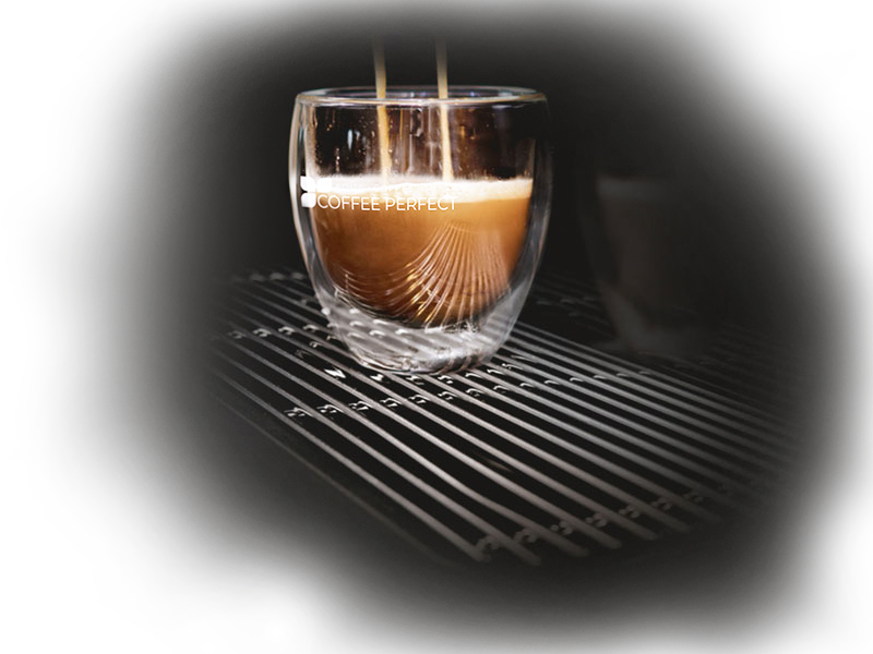 Frisch gebrühter Espresso läuft in ein doppelwandiges Glas mit coffee perfect Logo.