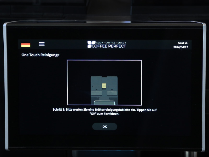 Display zeigt Einlegen einer Brueheinheit-Reinigungstablette und Bestaetigung mit 'OK'.