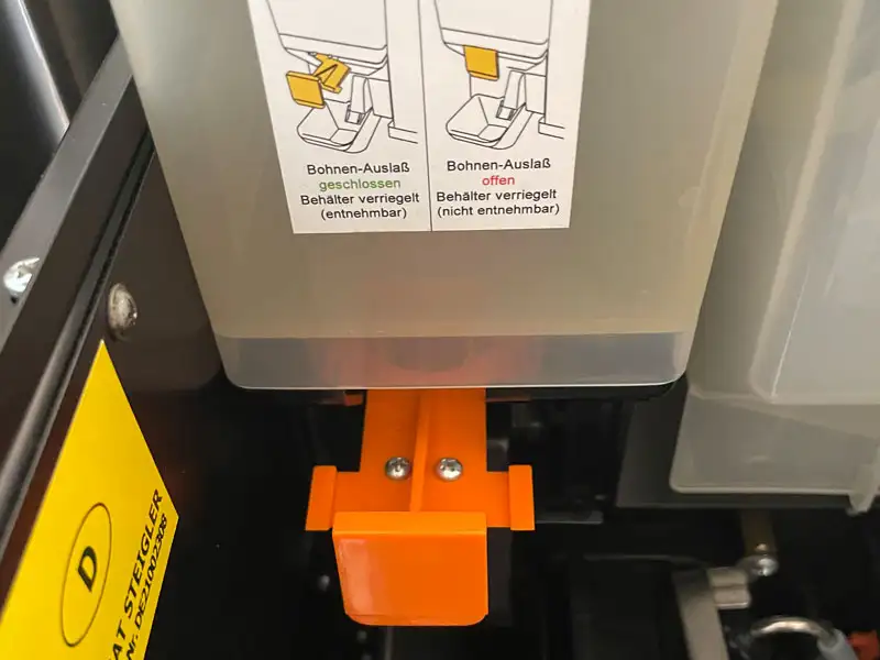 Nahaufnahme des orangefarbenen Bohnen-Auslasses mit Verriegelungsmechanismus.