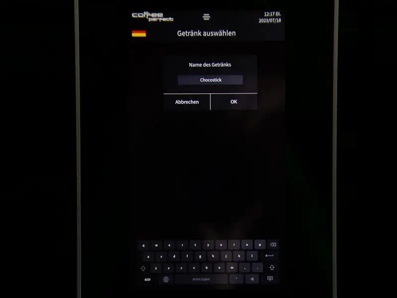 Display eines Kaffeevollautomaten mit Eingabe des Getraenkenamens 'Chocostick'.