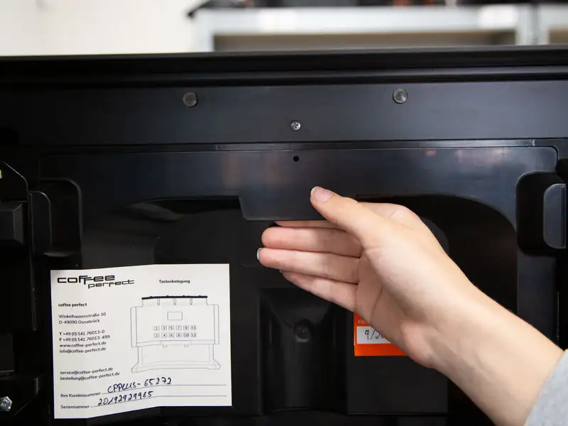 Hand hebt obere Abdeckung der Kaffeemaschine an, um Zugang zur Elektronik zu erhalten.