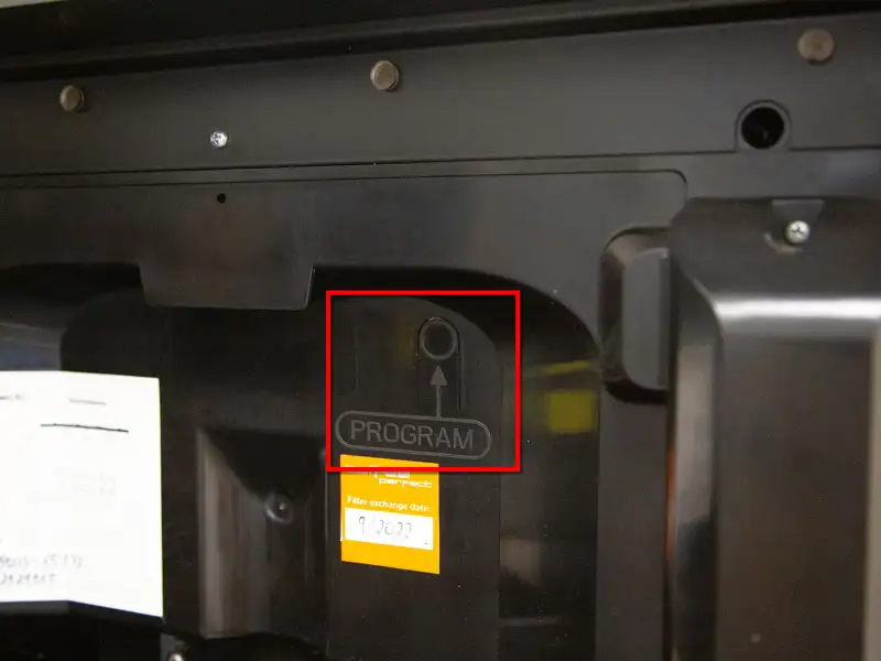 Markierte Programmtaste mit Beschriftung 'PROGRAM' an der Rueckwand der Kaffeemaschine.